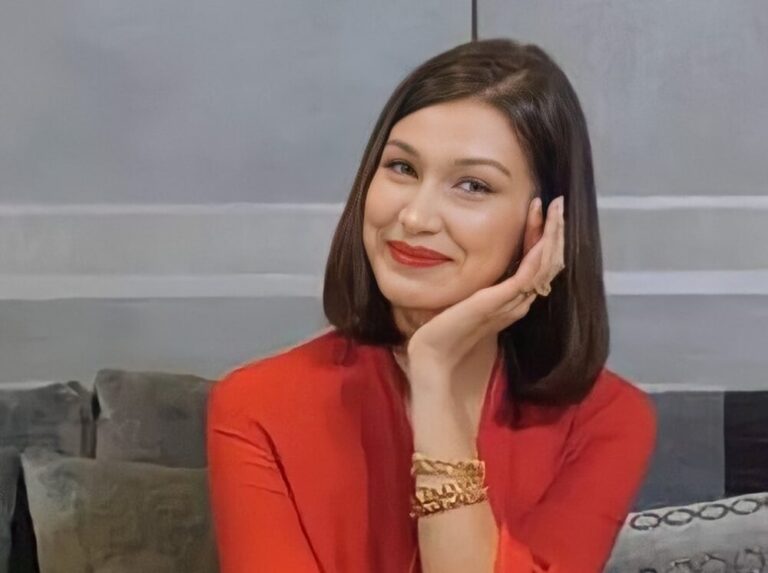 uśmiechnięta Bella Hadid w czerwonym ubraniu siedzi