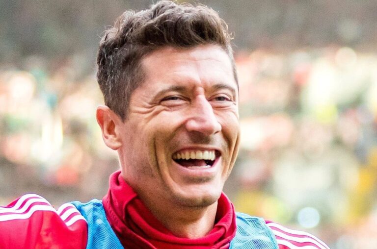 Robert Lewandowski uśmiecha się na meczu w czerwonej bluzie